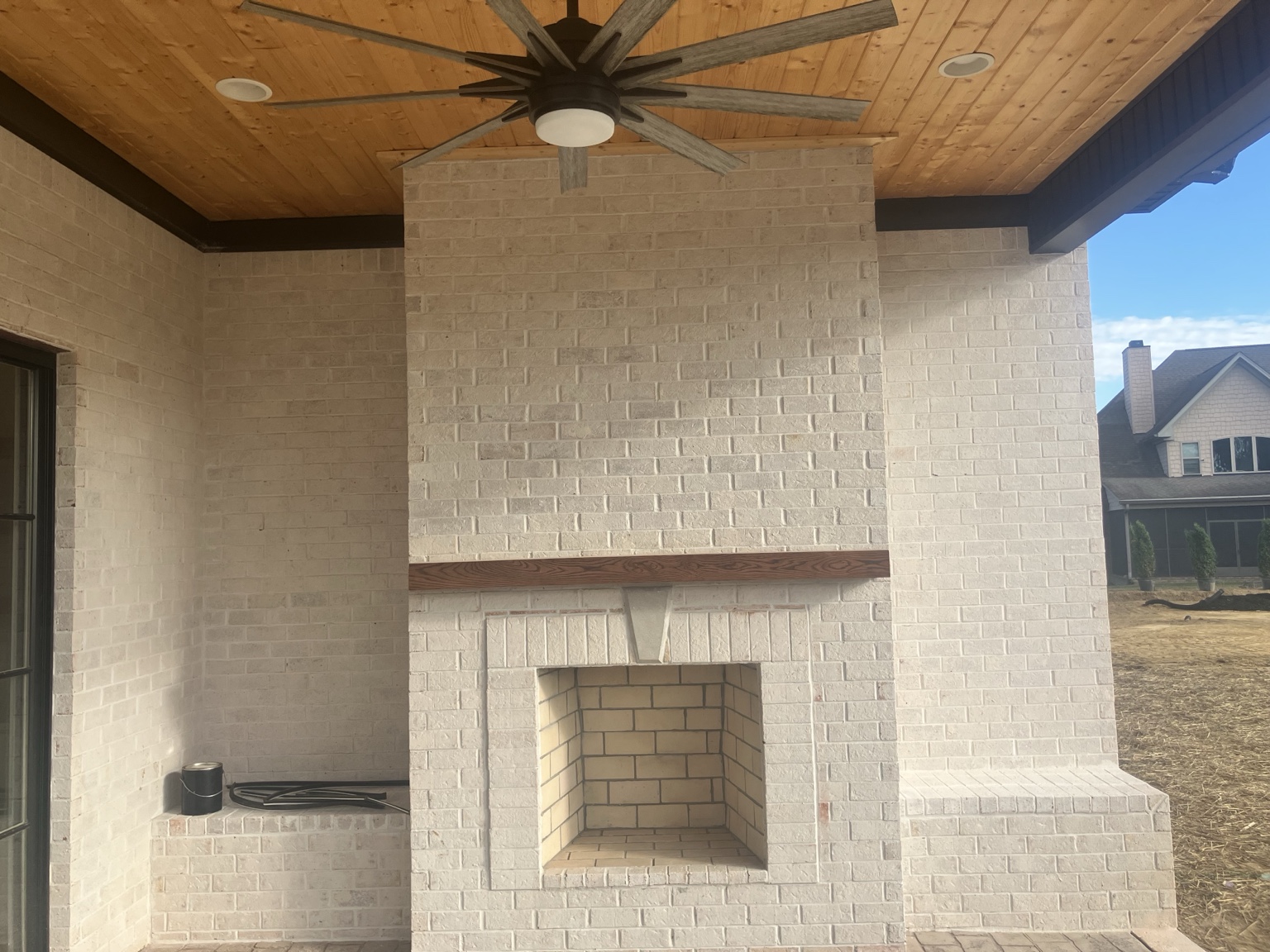 Covered outdoor living area with brick fireplace and wood ceiling